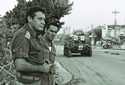 מפקד אוגדה 162 ,תא״ל מנחם עינן )משמאל(, ומפקד אוגדה 96 ,תא״ל ימוס ירון, צופים בנסיגת כוחות האויב מביירות. על הכביש: בי-טי-אר-60 סורי ועליו תמונות הנשיא הסורי חאפז אל-אסד. קרדיט: דובר צה״ל